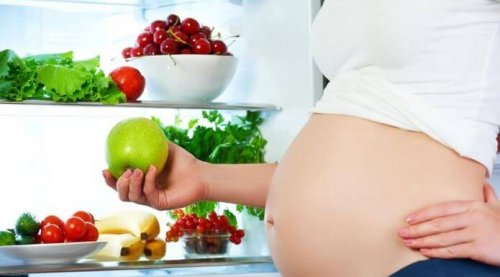 Pregnant woman standing by refrigerator fruits and vegetables inside pregorexia