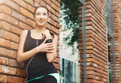 Woman outside running taking a break next to a brick building listening to music