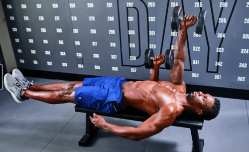Man laying on bench in gym doing a single-arm larsen press with dumbbells