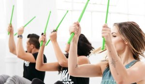 Three people using green drumsticks to work out