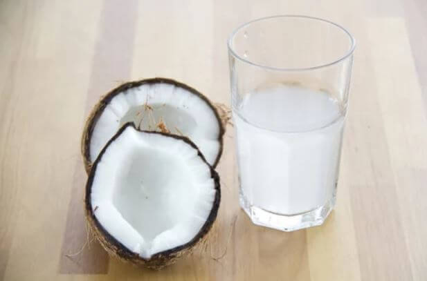 A coconut next to a glass of coconut oil