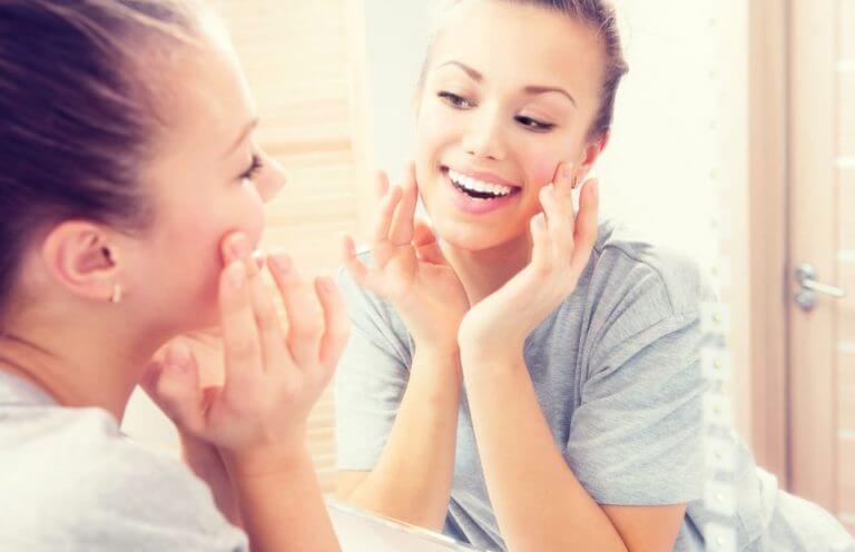 A happy woman looking in the mirror and noticing the benefits of safflower oil