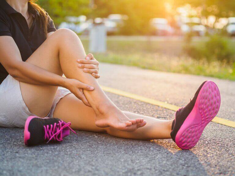 A woman sitting on the road and rubbing her leg to alleviate the pain from a muscle strain