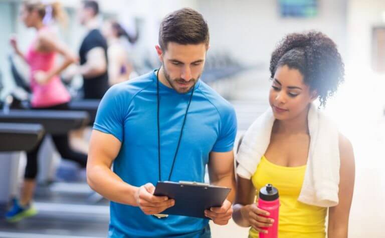 A girl going over her wight training program with a personal trainer