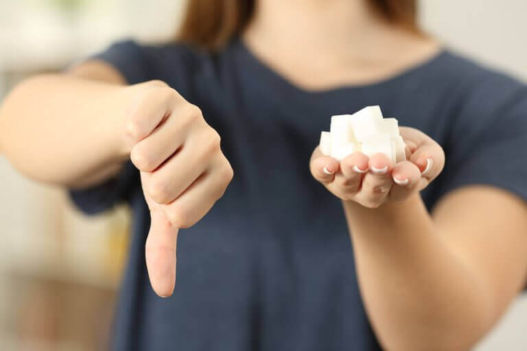 A woman holding sever sugar cubes in one hand and making a thumbs down sing with the other
