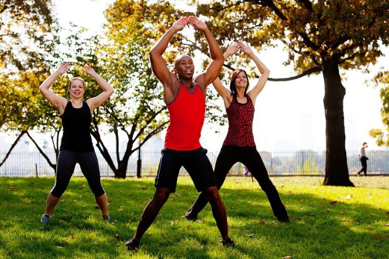 Three people doing jumping jacks in a park