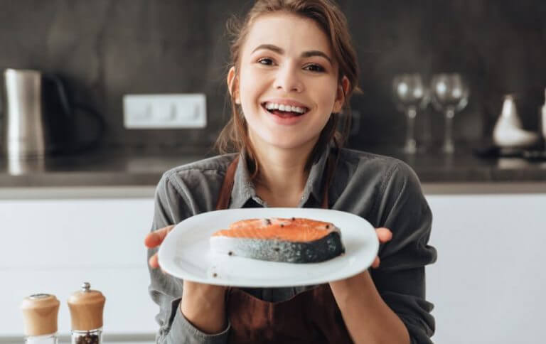Woman holding a piece of salmon to exemplify good examples of natural proteins
