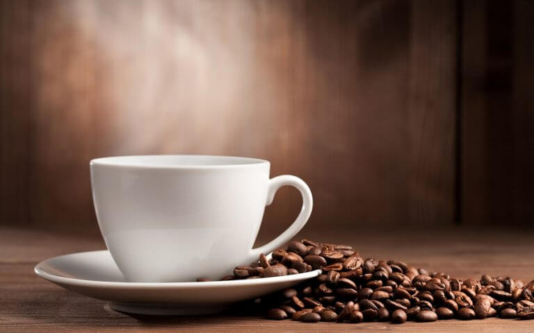 A steaming cup of coffee next to a bunch of coffee beans