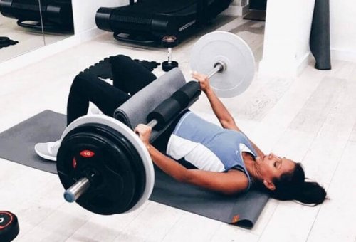 Woman at the gym using a weighted bar for a hip thrust and glute bridge