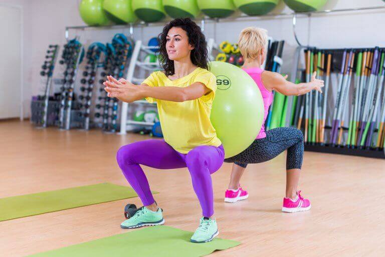 Two women doing squats with a fit ball