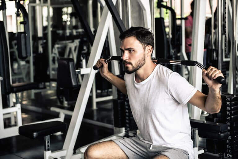 A man using the machine that allows you to do chest pulls, which supports the text describing this.