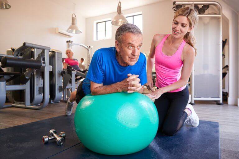 A personal trainer helping an older man to use a fit ball in his training routine