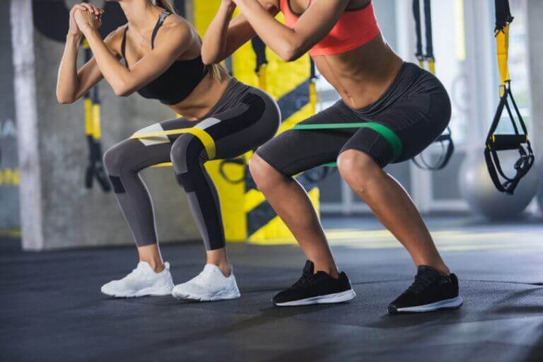 Two women doing squats with elastic bands around their thighs