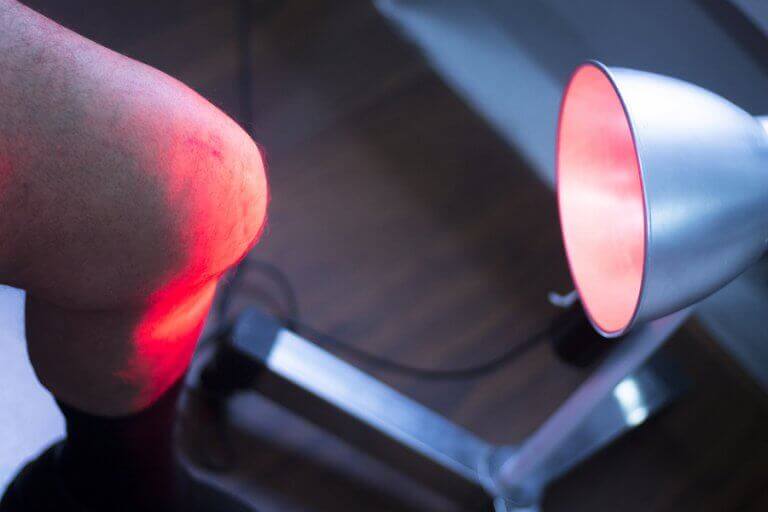 A man applying heat to his knee with a lamp