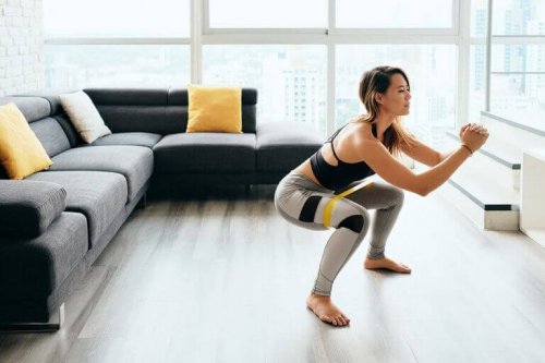 Woman doing squats in front of her tv to counteract the negative impact of sitting down at work