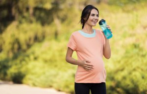 A pregnant woman walking and drinking water.
