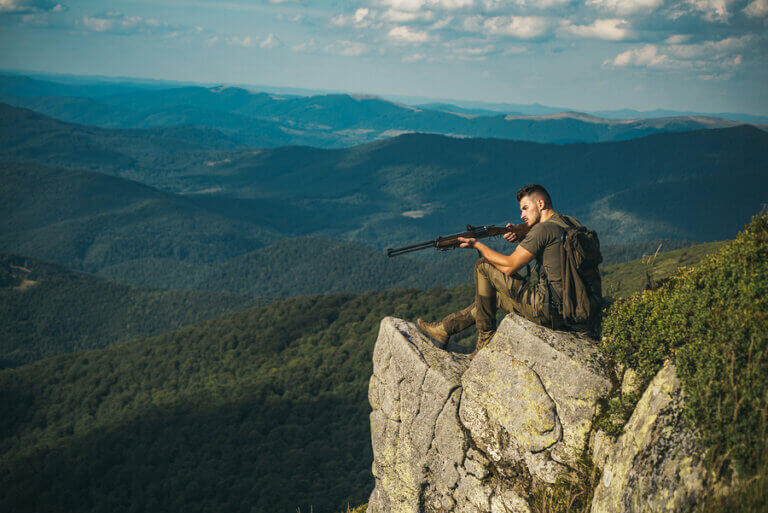 A man holding a hunting rifle on top of a mountain