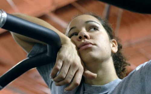 A tired woman leaning on gym equipment.