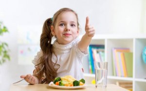 A girl eating pasta with vegetables.