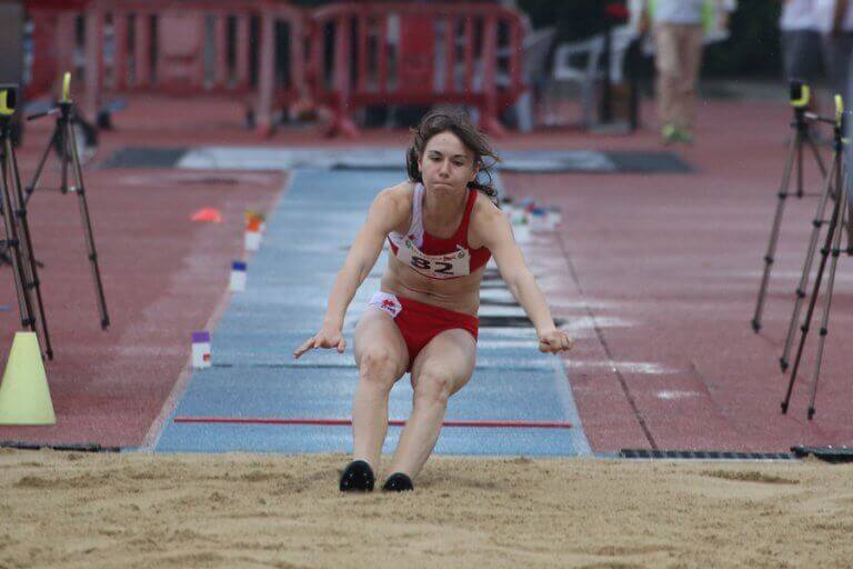 An athlete that is part of the Spanish Athletics Federation performing a long distance jump during an official competition