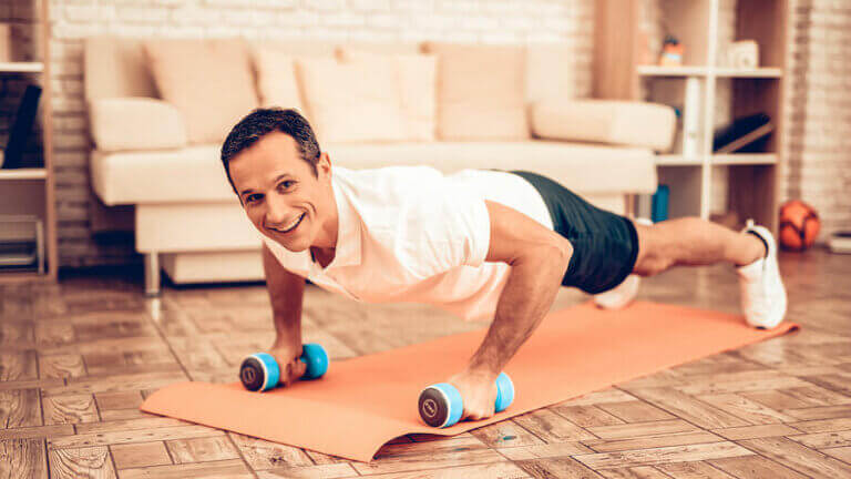 A smiling man doing dumbbell pushups at home