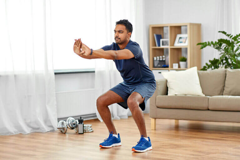A man doing easy CrossFit exercises such as squats in the middle of his living room