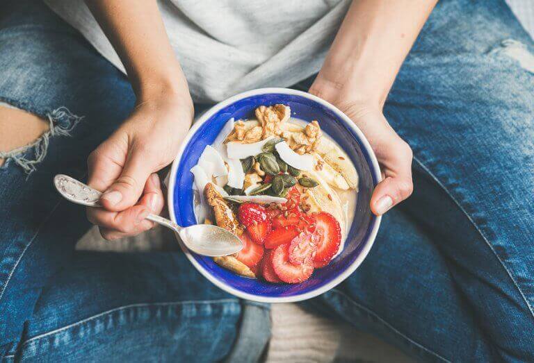 A person eating a bowl of fresh fruit and yogurt to keep their intestinal microbiota healthy