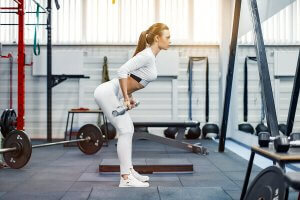 A woman in a gym deadlifting a bar.