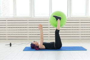 A woman lying down with a Swiss ball between her feet.