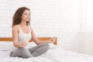 A woman meditating on her bed.