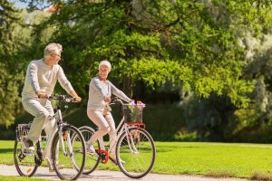 Two elderly people riding bikes outside.
