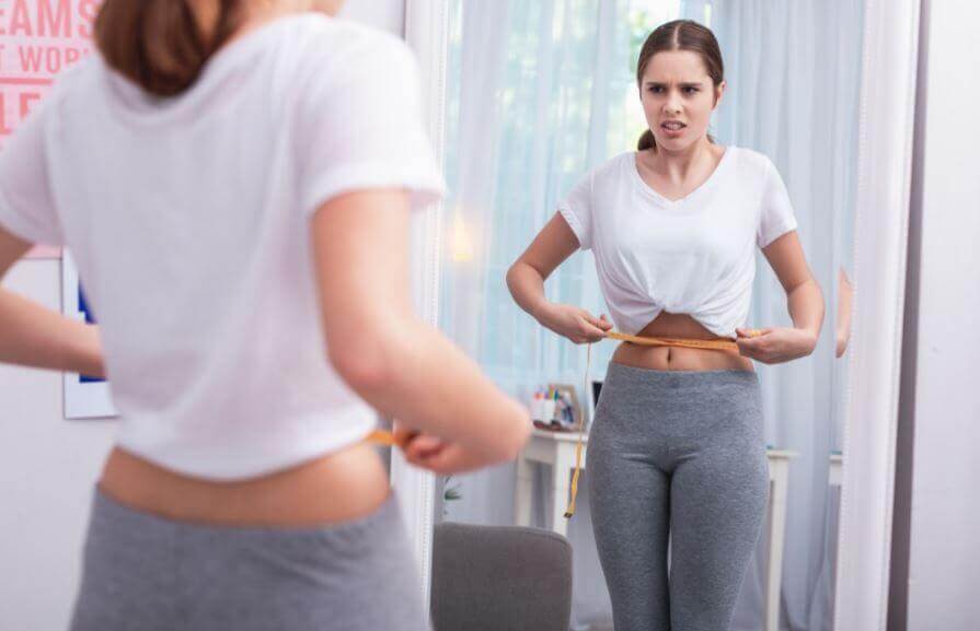 A woman measutring her waist in front of the mirror