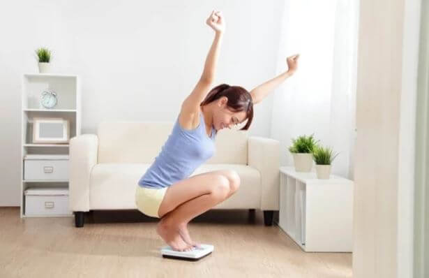 A woman stepping on a scale and celebrating that she was able to lose weight by running