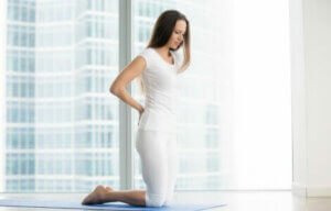 A woman on a yoga mat feeling her lower back.