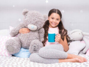 A girl on her bed drinking milk with her teddy.