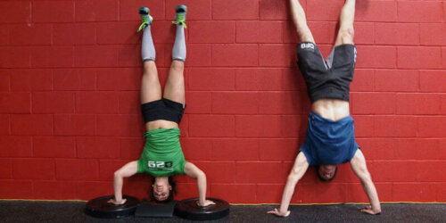 Two men doing a handstand against a wall.