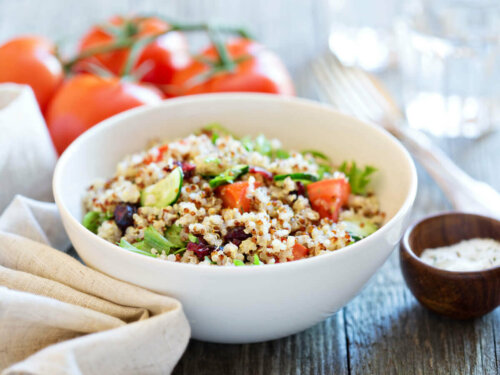 A bowl of quinoa salad with tomatoes behind it.