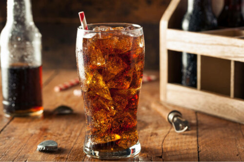 A cola soft drink in a glass with bottles in the background.