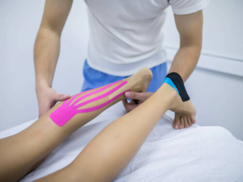 Physical therapist taping patient's leg with neuromuscular bandage.