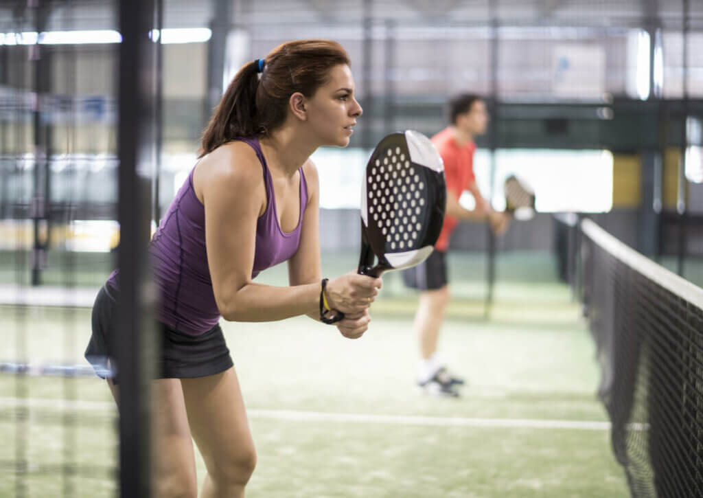 woman playing paddle tennis about to serve the ball; paddle tennis and tennis