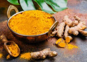 A bowl of turmeric next to some turmeric root.