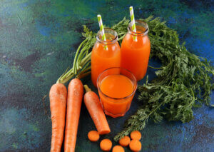 Jars and glasses of carrot juice next to some carrots.