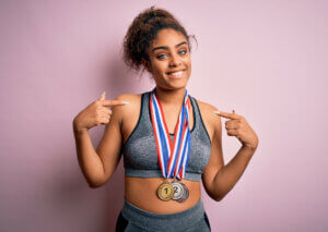 Woman wearing medals pointing at herself.