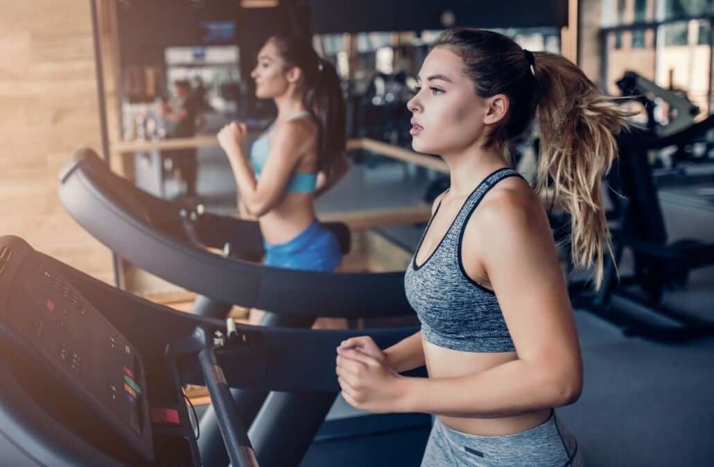 Two women running on treadmills in a gym.