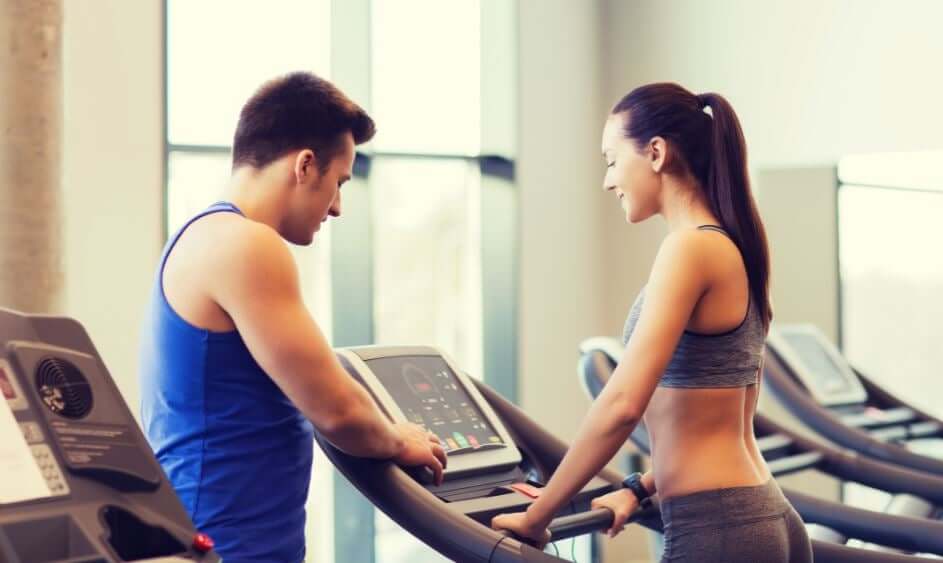 A personal trainer setting up a treadmill for a woman.