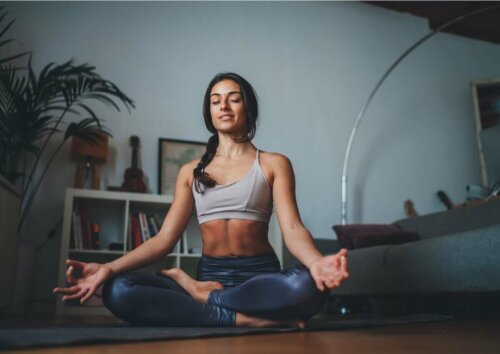 woman practicing yoga, sitting on living room floor in gym wear