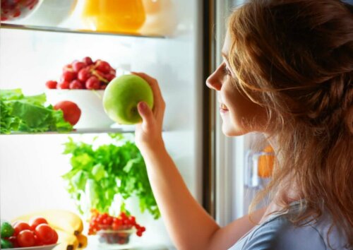 woman opening fridge to get a little snack an apple with loads of other fruit and veg in the fridge
